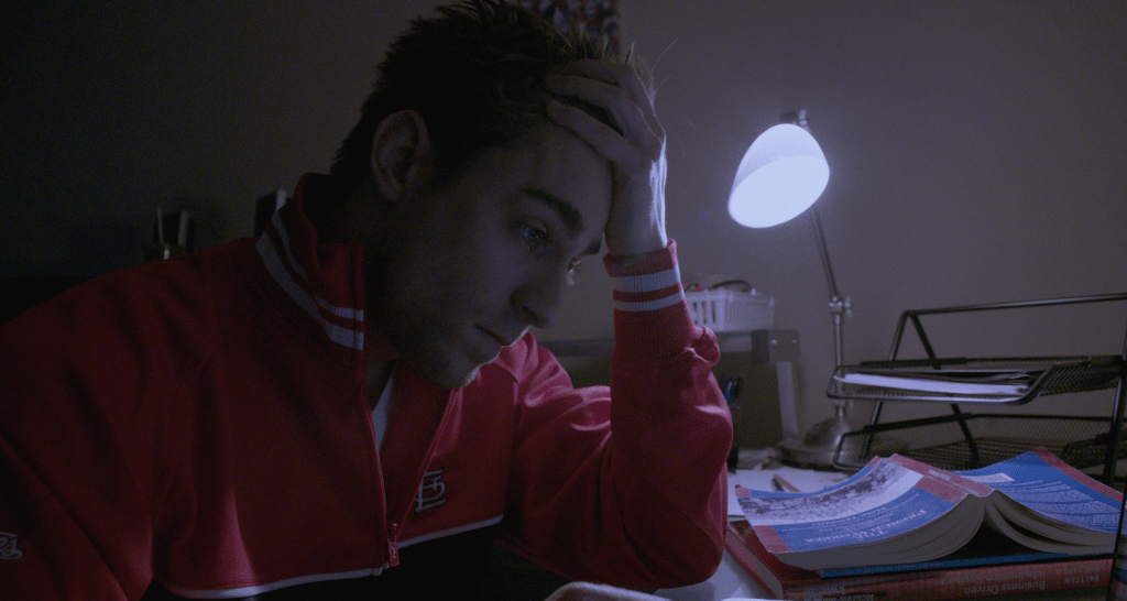 Drew Dawson (Luke Guldan) holding his forehead while studying